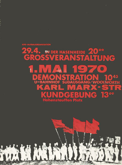 Ein schwarzes Plakat mit weißem und rotem Text kündigt eine Großveranstaltung am 29. April und eine Demonstration am 1. Mai 1970 in der Karl-Marx-Straße an. Am unteren Rand ist eine rote Grafik mit Fahnen und einer Menschenmenge abgebildet.