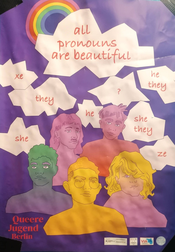 Ein Poster mit lila Hintergrund zeigt fünf illustrierte, bunte Porträts von Personen in verschiedenen Farben: grün, rosa, orange, gelb und pink. Oben links ist ein Regenbogen. In weißen Sprechblasen stehen Pronomen wie "xe", "they", "he", "she", "ze" und die Phrase "all pronouns are beautiful" in roter Schrift. Unten links steht "Queere Jugend Berlin" ebenfalls in Rot.