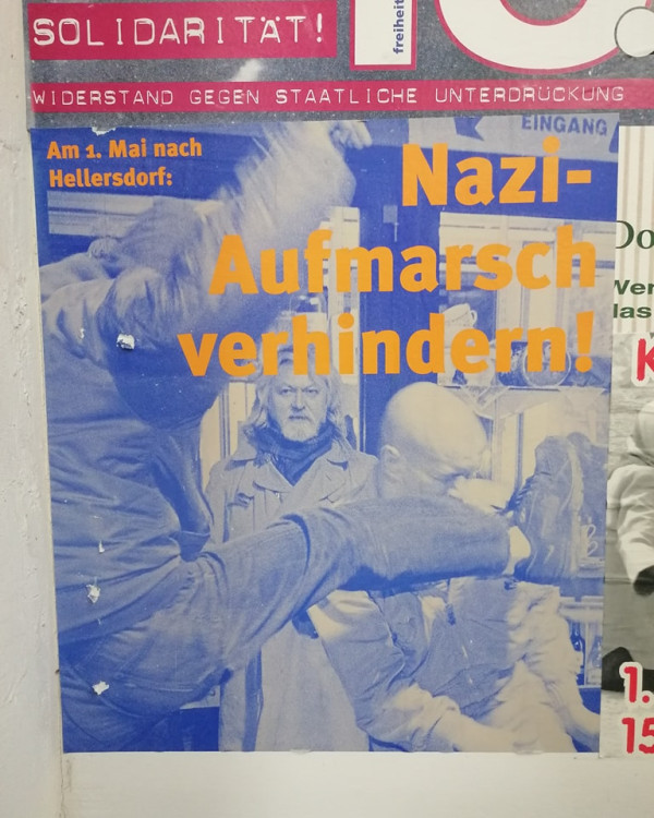 Das Plakat zeigt ein blau gefärbtes Bild eines Mannes in einem Mantel, umgeben von einer Auseinandersetzung. Der Text lautet "Solidarität! Widerstand gegen staatliche Unterdrückung. Am 1. Mai nach Hellersdorf: Nazi-Aufmarsch verhindern!" in rot und orange.