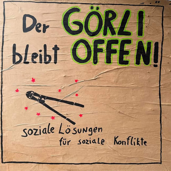 Auf einem braunen Plakat mit schwarzer Handschrift steht fett "Der Görli bleibt offen!", wobei "Görli offen" grün umrandet ist. Darunter befindet sich eine Abbildung von Bolzenschneidern und der Text "soziale Lösungen für soziale Konflikte" mit roten Sternen.