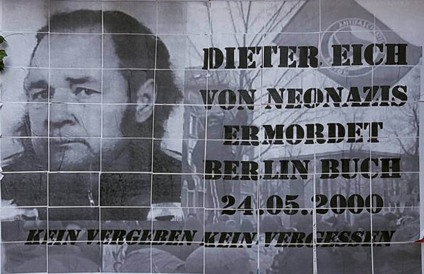 Ein schwarz-weißes Plakat zeigt das Porträt eines Mannes. Rechts neben dem Bild steht in fetter Schrift: "Dieter Eich von Neonazis ermordet Berlin Buch 24.05.2000". Darunter in etwas kleinerer Schrift: "Kein Vergeben Kein Vergessen". Der Hintergrund zeigt eine Fahne der Antifaschistischen Aktion und Bäume.