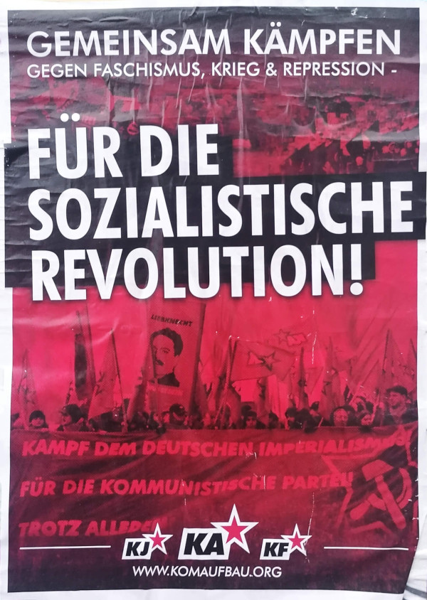 Plakat mit rotem Hintergrund, das einen Protest zeigt. Text: "GEMEINSAM KÄMPFEN GEGEN FASCHISMUS, KRIEG &amp; REPRESSION - FÜR DIE SOZIALISTISCHE REVOLUTION!" Website: www.komaufbau.org.