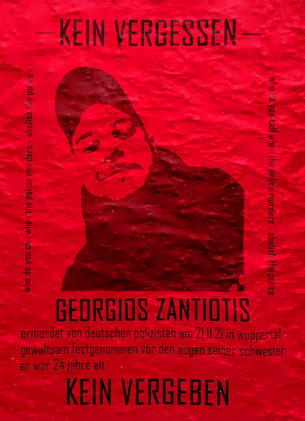 Ein rotes Poster mit der schwarzen Silhouette eines Mannes, der eine Mütze trägt. Oben steht „Kein Vergessen“. Seitlich steht in Englisch „Who do you call when the police murders - abolish the police“. Unten in großer Schrift „Georgios Zantiotis“. Darunter: „ermordet von deutschen Polizisten am 21.11.21 in Wuppertal gewaltsam festgenommen vor den Augen seiner Schwester er war 24 jahre alt“. Am unteren Rand steht „Kein Vergeben“.
