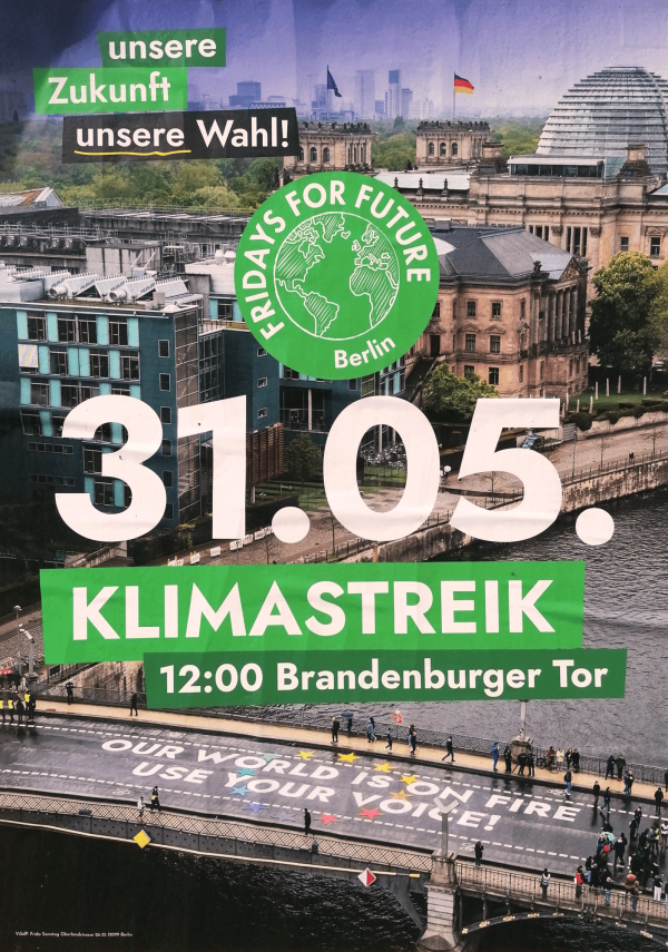 Ein Poster mit dem Berliner Regierungsviertel im Hintergrund. Oben links steht "unsere Zukunft unsere Wahl!" in grün-schwarzen Kästchen. Zentral ist das Datum "31.05." in großen weißen Zahlen. Darunter steht "Klimastreik" und "12:00 Brandenburger Tor" in weiß auf grünem Hintergrund. Ein grünes Logo zeigt die Erdkugel mit dem Text "Fridays For Future Berlin". Unten ist eine Straße mit der Aufschrift "Our world is on fire, use your voice!" zu sehen.
