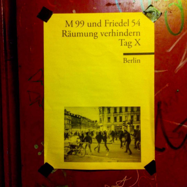 Gelbes Plakat mit schwarzem Text: "M 99 und Friedel 54 Räumung verhindern Tag X Berlin". Das Bild zeigt Menschen in einer Straße der Stadt. Das Plakat ist an eine rote, mit Graffiti beschmierte Wand geklebt.