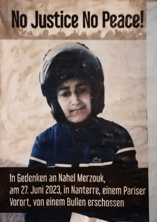 Das Poster zeigt ein Bild eines jungen Mannes mit einem schwarzen Helm und einer blauen Jacke. Oben steht in schwarzer Schrift auf beigem Hintergrund: "No justice no peace!" Unten befindet sich ein schwarzer Balken mit weißem Text: "In Gedenken an Nahel Merzouk, am 27. Juni 2023, in Nanterre, einem Pariser Vorort, von einem Bullen erschossen." Der Hintergrund ist beige und strukturiert.