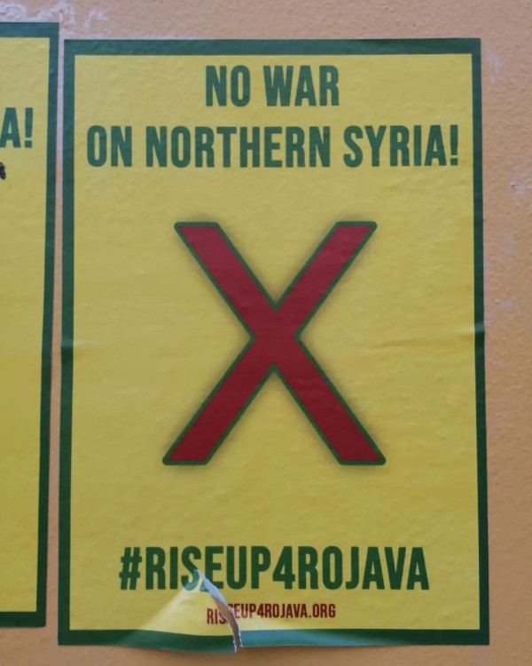Gelbes Plakat mit grünem Rand, auf dem ein großes rotes "X" zu sehen ist. Der Text lautet "Kein Krieg gegen Nordsyrien!" und "#riseup4rojava". Link zur Website: riseup4rojava.org.