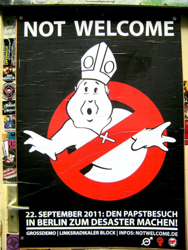 Ein schwarzes Plakat zeigt eine Cartoon-Figur, die dem Papst ähnelt, inmitten eines roten Verbotssymbols. Der Text lautet "Not Welcome" und beschreibt einen Protest am 22. September 2011 in Berlin.
